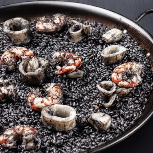 Creative concept photo of  paella 
sea food and black rice on plate on black background.