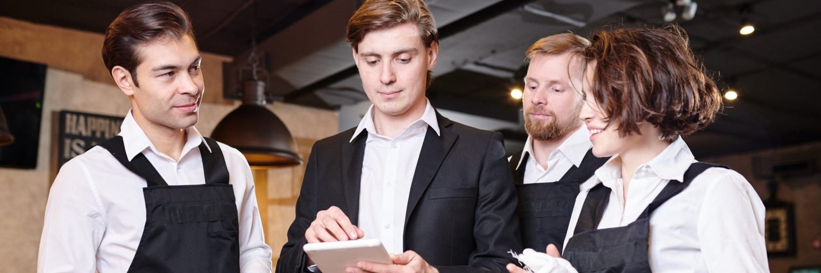 Serious confident handsome young restaurant manager using tablet while dividing responsibilities among waiters in modern establishment